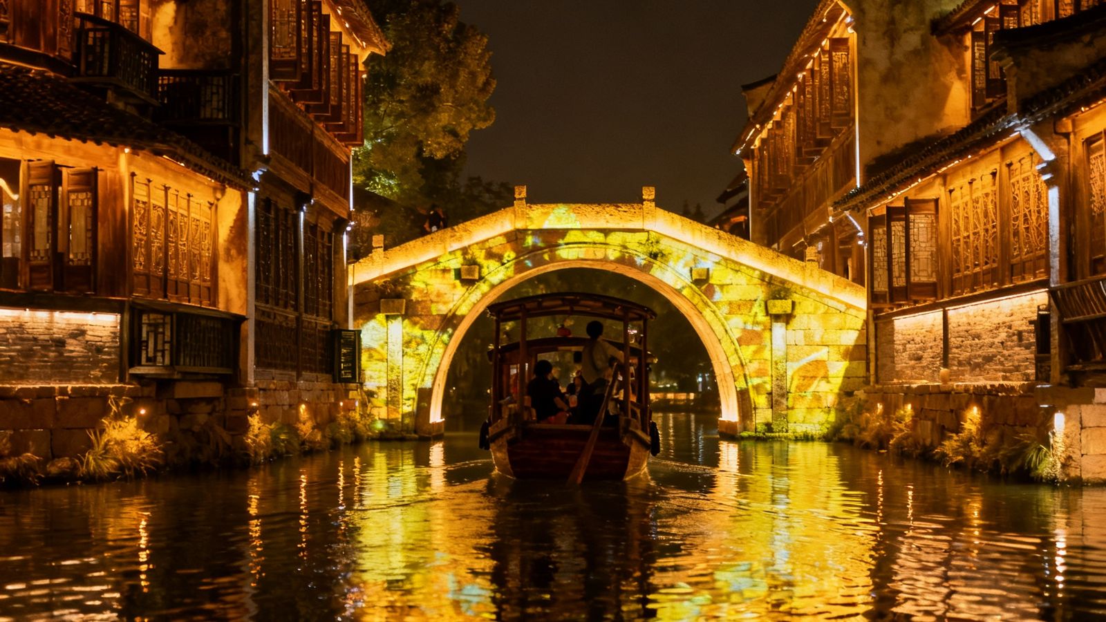 乌镇西栅景区夜景，河面上漂浮着柔和的投影灯光倒影，两岸古建筑被暖金色灯光勾勒出轮廓，一座石拱桥下穿过的游船载着游客欣赏两岸光影秀。